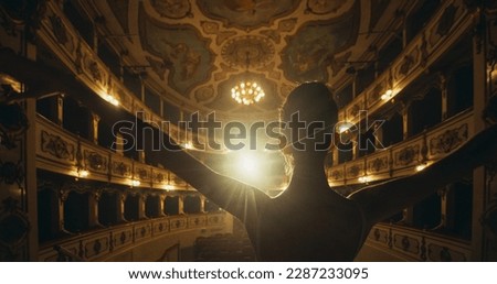 Cinematic Back View of Young Classical Ballet Female Dancer Standing on Classic Theatre Stage with Spotlights for the Curtain Call. Graceful Performer Accepting the Audiences' Applause for her Talent Royalty-Free Stock Photo #2287233095