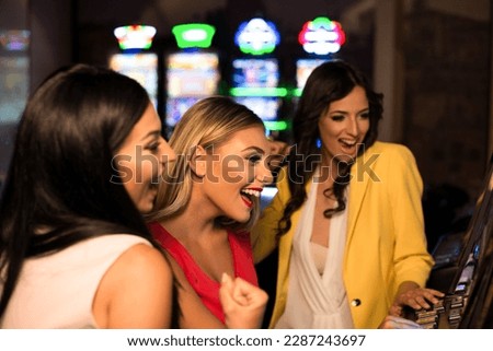 Beautiful and Well Dressed Girls Playing Automat Machine in the Casino and Celebrate Royalty-Free Stock Photo #2287243697