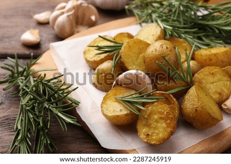 Delicious baked potatoes with rosemary and garlic on parchment paper, closeup
