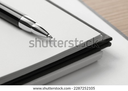 Ballpoint pen and notebooks on wooden table, closeup