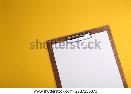 Wooden clipboard with sheet of blank paper on yellow background, top view. Space for text