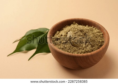Henna powder and green leaves on beige background, closeup. Natural hair coloring