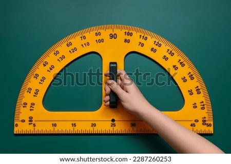 Woman holding protractor with measuring length and degrees markings near green board, closeup