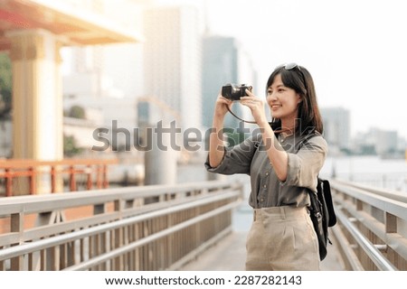 Young Asian woman backpack traveler using a camera in express boat pier on Chao Phraya River in Bangkok. Traveler checking out side streets.
