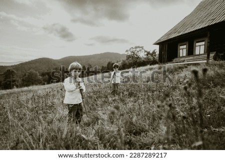 Little boys playing on woodwind wooden flutes - ukrainian sopilka on meadow of Carpathian mountain. Duet folk music concept. Kids in traditional embroidered shirts. High quality photo