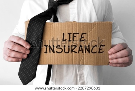 A disheveled business man holds up a cardboard sign with the words Life Insurance