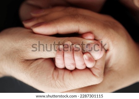 Close-up of the small hand of the child and the hand of the mother and father. A newborn baby after birth clings tightly to the finger of its parents. Professional macro photo on black background
