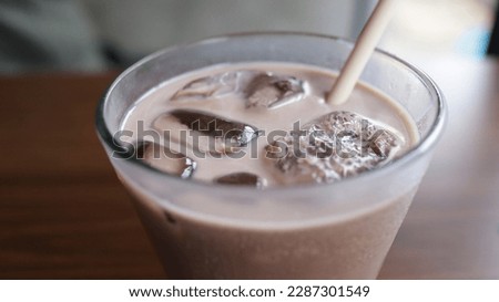 A glass of ice chocolate milk at a table with a straw.
