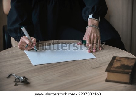 The hands of a young woman write on a blank sheet of paper on a wooden table. Mockup, copy space