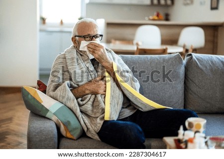 Shot of a sickly senior man blowing his nose with a tissue at home.  Royalty-Free Stock Photo #2287304617