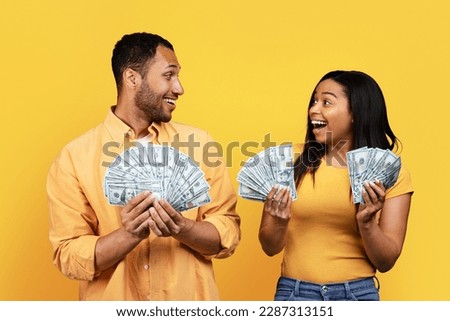 Cheerful shocked millennial african american man and woman hold a lot of cash, rejoice victory together isolated on yellow studio background. Cashback, money profit, win and people emotions