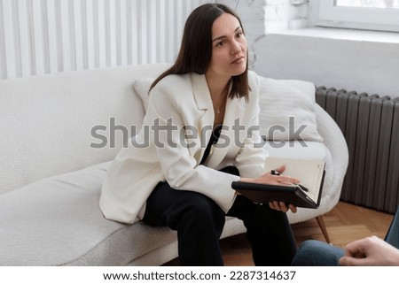 A female psychologist sitting on the sofa with a notebook in her hands and attentively listens to her clients at the reception during a family consultation Royalty-Free Stock Photo #2287314637