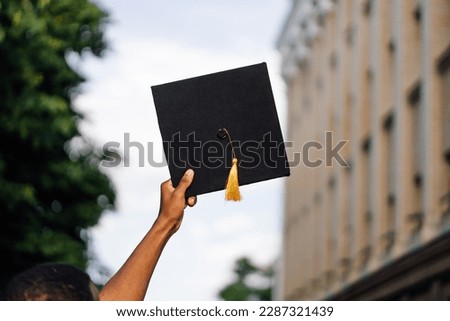 Photo back view of african american graduate from university standing outdoors and holding in hand black hat, blurred sky background, free copy space. Future career, graduation, young specialist.