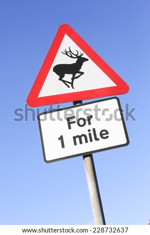 Red and white triangular warning road sign indicating the danger of deer on the road for one mile. 