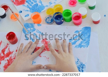 Children dip hand in paint and apply it to white sheet and palm with fingers is displayed on paper. Palms of different colors