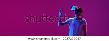 One young boy wearing VR glasses over pink background in neon light. Youth and virtual lifestyle of future. Concept of games, digitalization and technology. Banner with copy space for text, ad