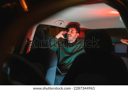 One young man is working from car in backseat while using laptop and mobile phone to work during the night Royalty-Free Stock Photo #2287344961