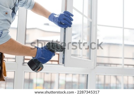 handyman adjusting white pvc plastic window indoors. worker using screwdriver to repair upvc window. homework maintenance. Royalty-Free Stock Photo #2287345317