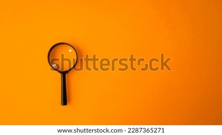 Magnifying glass, magnifier in a black frame on an orange background.  Research concept, magnification of objects.  Flat top view.  Space for copy text.