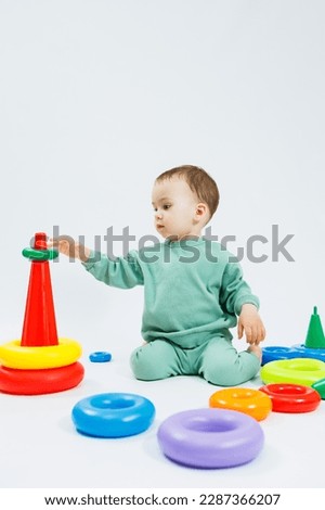 Cheerful little boy sitting with plastic educational toys on a white background. Child and toys for development. Development of children's motor skills.