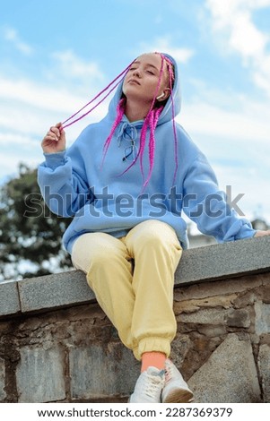 Portrait of a caucasian teenage girl with pink braids using wireless headphones in the park.Technology,summer concept.Generation Z style.