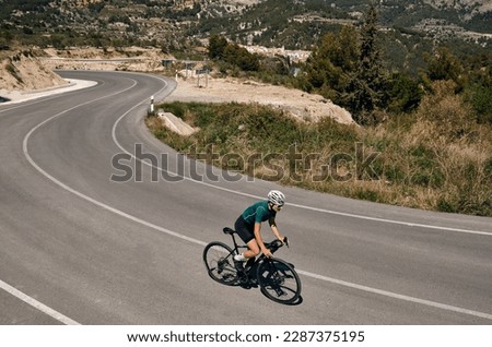 Woman cyclist riding a gravel bike with a view of the spanish mountains.Fit athlete wearing sportswear and helmet.Sports motivation image.Good road for cycling.Guadalest,Alicante, Spain. Royalty-Free Stock Photo #2287375195