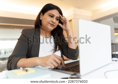 Stressed tired Indian businesswoman using laptop computer working project in office. Failure business. Serious freelancer missed deadline sitting at workplace 