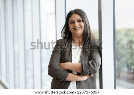Confident smiling mature Indian businesswoman with arm crossed standing in modern office. Portrait of happy asian worker wearing stylish suit looking at camera indoors. Successful business concept  Royalty-Free Stock Photo #2287376057