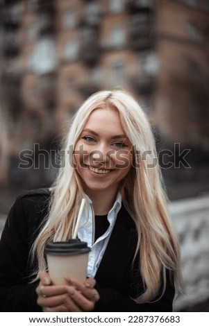 happy girl student drinks coffee before studying on city building background. woman smiling and looking at camera