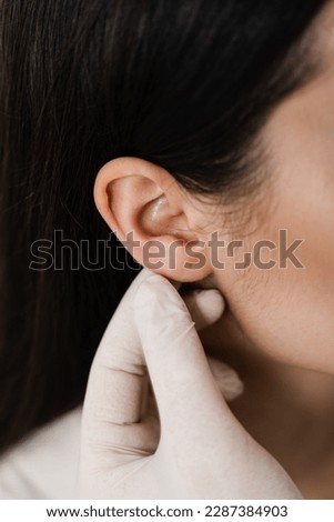 Otoplasty ear surgery close-up. Surgeon doctor examines girl ears before otoplasty cosmetic surgery. Otoplasty surgical reshaping of pinna and ear