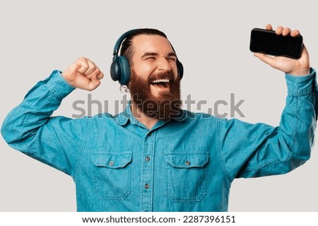Handsome bearded man is having fun while listening to the music in headphones.