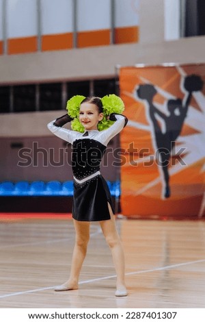 A beautiful smiling girl, a child, a cheerleader sportswoman in a uniform, a colored dress, dances, showing complex elements of gymnastics in the gym. Photography, portrait, sport concept.