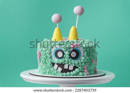 Monster theme cake on the turquoise background. Funny birthday cake with turquoise fluffy cream cheese frosting. Spooky monster pastry with edible fur. Happy Halloween party