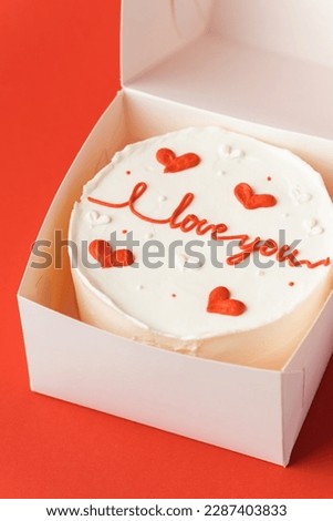 Korean style bento cake in a white gift box on the red festive background. Little cake with I love you inscription. Happy Valentine's Day