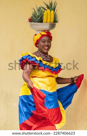 Happy smiling Palenquera fresh fruit street vendor dancing in the Old Town of Cartagena de Indias, Colombia. Cheerful Afro-Colombian woman in traditional clothing, Colombian culture and lifestyle. Royalty-Free Stock Photo #2287406623