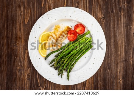 Fish dish - fried cod with green asparagus, lemon and fresh tomatoes on wooden table 