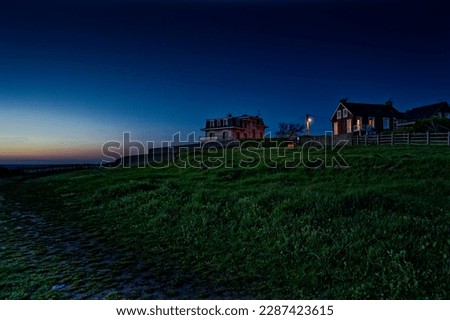 Picturesque night landscape with French houses and huts with luminous windows. Located on a hill with green grass on the ocean, in the English Channel. Royalty-Free Stock Photo #2287423615