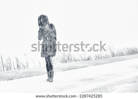A snowstorm. People walk down the street during a snowstorm. Heavy snowfall.  against the background of a cold urban landscape