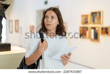 Portrait of an interested visitor girl with an information booklet, viewing an exhibit standing in an art gallery Royalty-Free Stock Photo #2287431887