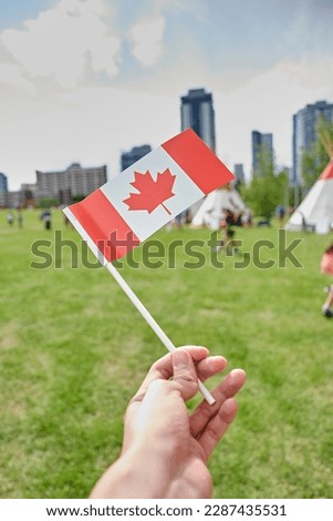 Canada flag waving in Calgary Riverwalk park full of people in summer buildings in background clear sky large clean green grass calm woman holding flag