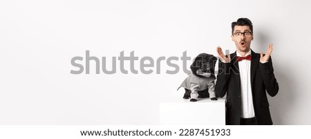 Animals, party and celebration concept. Image of dog owner and cute pug in costumes suits staring surprised at camera, reacting on promo offer, white background.