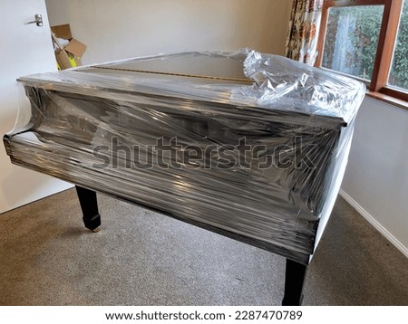 Glossy black grand piano partially covered in plastic wrap in preparation for removal by furniture moving company Royalty-Free Stock Photo #2287470789