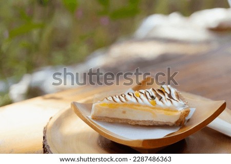 Piece of Lemon cheesecake tart slice with fresh lemon curd meringue burnt on wooden dish and table. Delicious and sweet dessert.