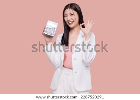 Young Asian woman feel happy with OK hand signal hold in hands calculator isolated on pastel pink background studio portrait.