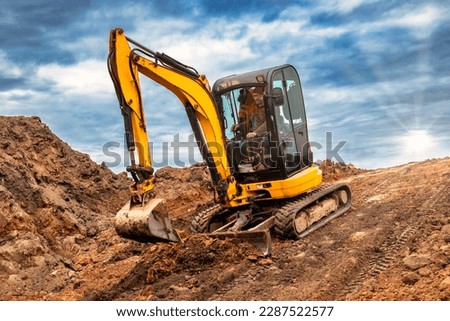 Mini excavator at the construction site on the edge of a pit against a cloudy blue sky. Compact construction equipment for earthworks. An indispensable assistant for earthworks Royalty-Free Stock Photo #2287522577