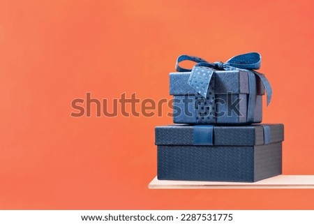 Two Luxury gift boxes with a blue bow on coral background. Side view on shelf. Fathers day or Valentines day gift for him. Corporate gift concept or birthday party. Festive sale copy space banner Royalty-Free Stock Photo #2287531775