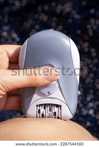 Woman using personal electrical epilator on herself at home. Hair removal electric device being used by a lady on her leg for smooth skin