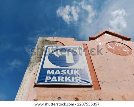 Arrow sign for parking "enter parking or masuk parkir" stuck to the wall on a hot day