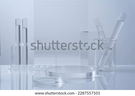 Science and medical background with transparent round podium, lab glassware filled colorless liquid and ribbed acrylic sheets decorated on white background. Space for products presentation