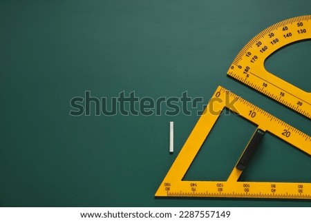 Protractor, triangle and chalk on green chalkboard, flat lay. Space for text